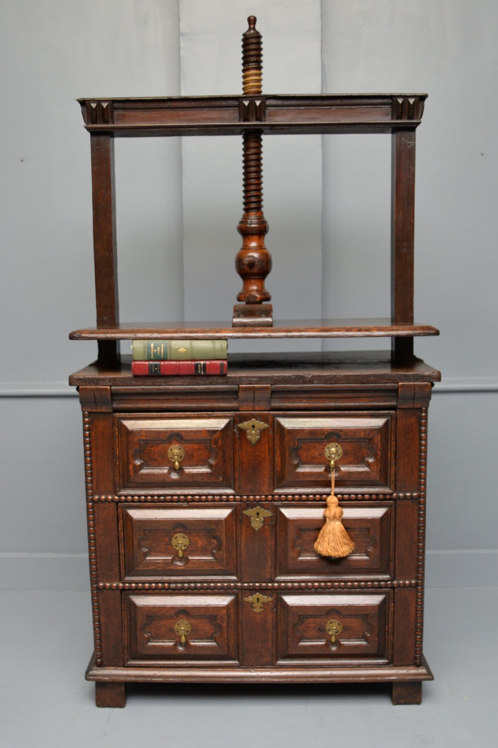 A 17th-century dark oak chest of drawers featuring geometric panelled drawer fronts and an integrated wooden screw linen press mounted on top. View VII