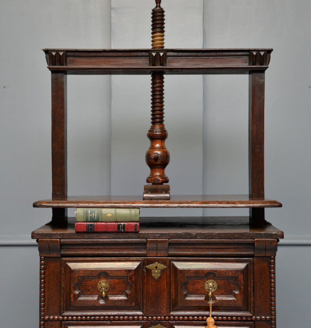 A 17th-century dark oak chest of drawers featuring geometric panelled drawer fronts and an integrated wooden screw linen press mounted on top. View IX