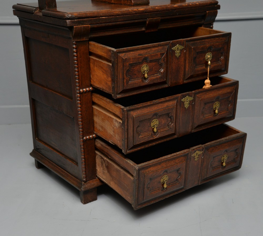 A 17th-century dark oak chest of drawers featuring geometric panelled drawer fronts and an integrated wooden screw linen press mounted on top. View XIV