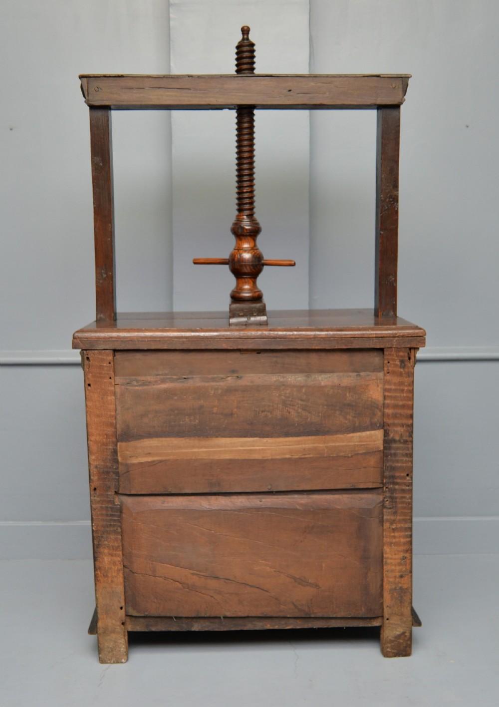 A 17th-century dark oak chest of drawers featuring geometric panelled drawer fronts and an integrated wooden screw linen press mounted on top. View XVII