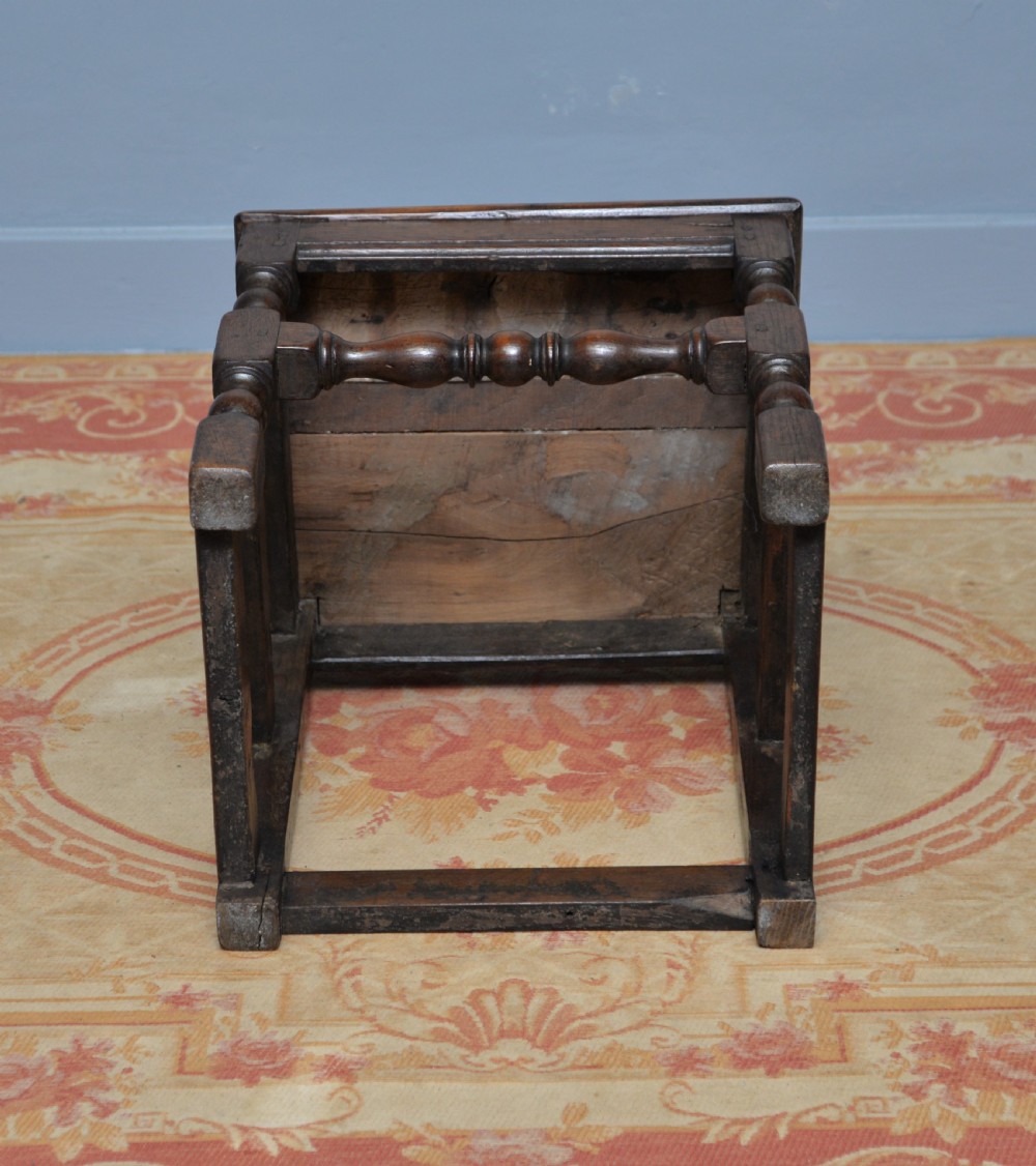A 17th-century dark oak side chair featuring a carved scroll crest rail, vertical slatted backrest, turned legs, and a solid wood seat. View XV