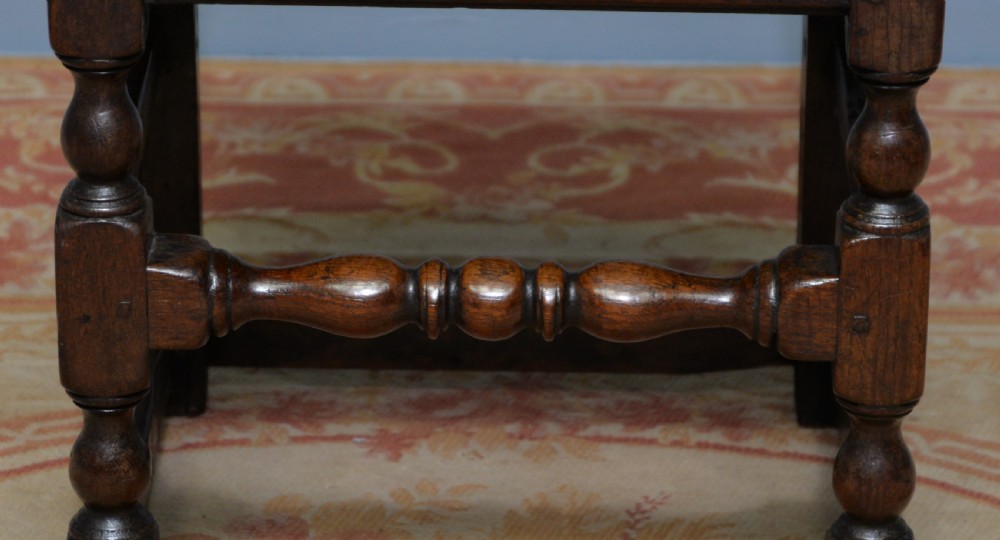 A 17th-century dark oak side chair featuring a carved scroll crest rail, vertical slatted backrest, turned legs, and a solid wood seat. View XIX