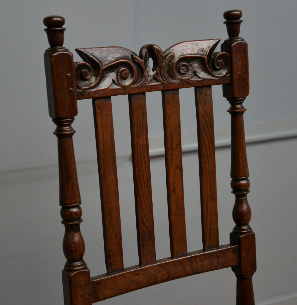 A 17th-century dark oak side chair featuring a carved scroll crest rail, vertical slatted backrest, turned legs, and a solid wood seat. View XXI