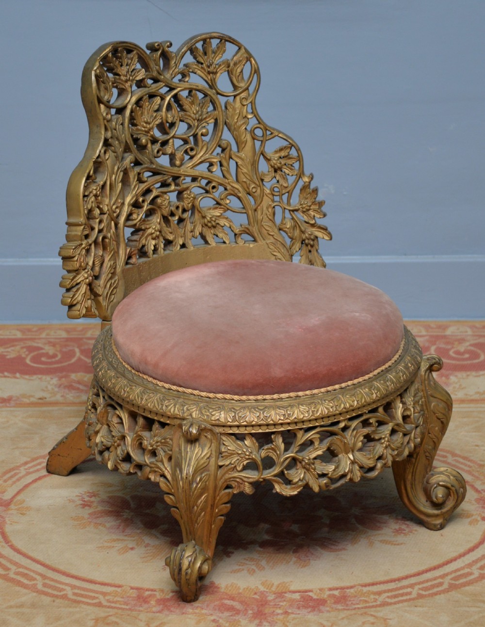 A low 19th-century Anglo-Indian side chair featuring openwork giltwood foliate carving and a round dusty pink velvet seat.