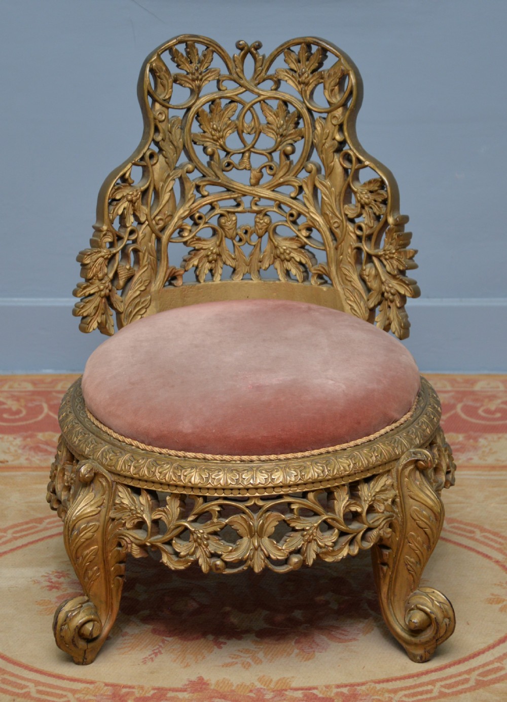 A low 19th-century Anglo-Indian side chair featuring openwork giltwood foliate carving and a round dusty pink velvet seat. View V