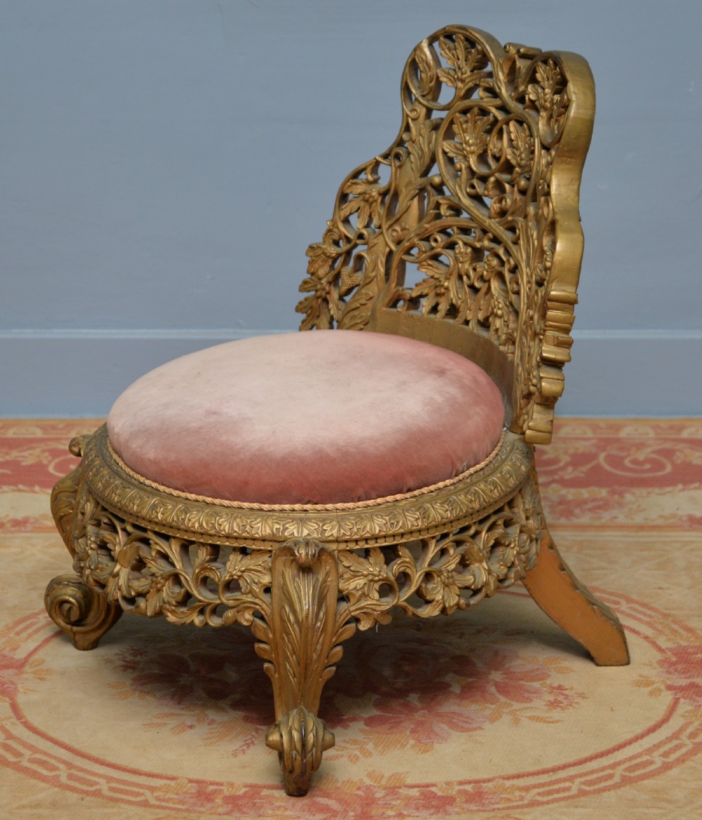 A low 19th-century Anglo-Indian side chair featuring openwork giltwood foliate carving and a round dusty pink velvet seat. View VII