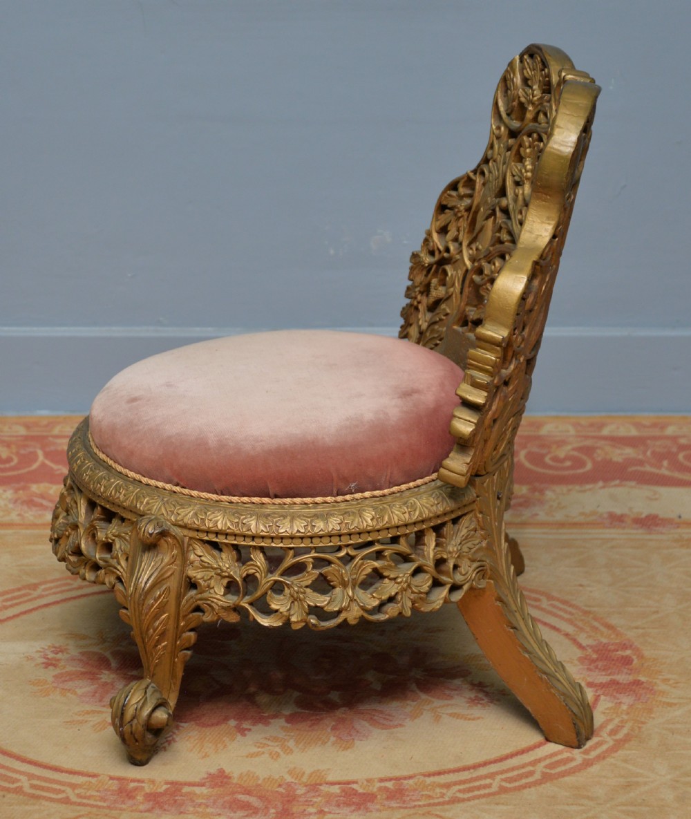 A low 19th-century Anglo-Indian side chair featuring openwork giltwood foliate carving and a round dusty pink velvet seat. View VIII