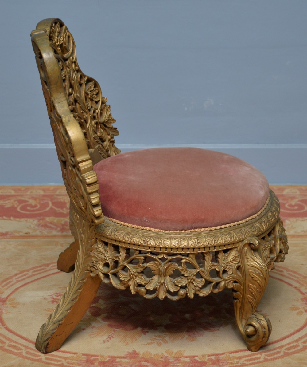 A low 19th-century Anglo-Indian side chair featuring openwork giltwood foliate carving and a round dusty pink velvet seat. View X