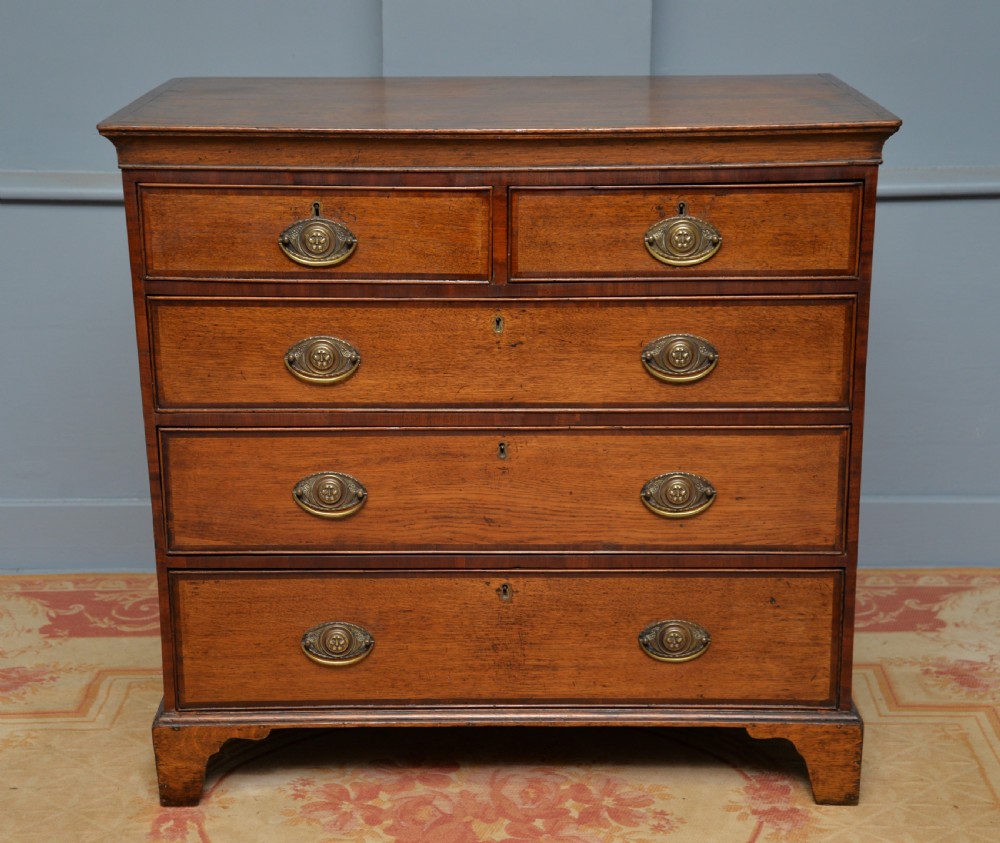 A George II solid oak chest of drawers featuring two short over three long graduated drawers with brass drop handles and bracket feet.