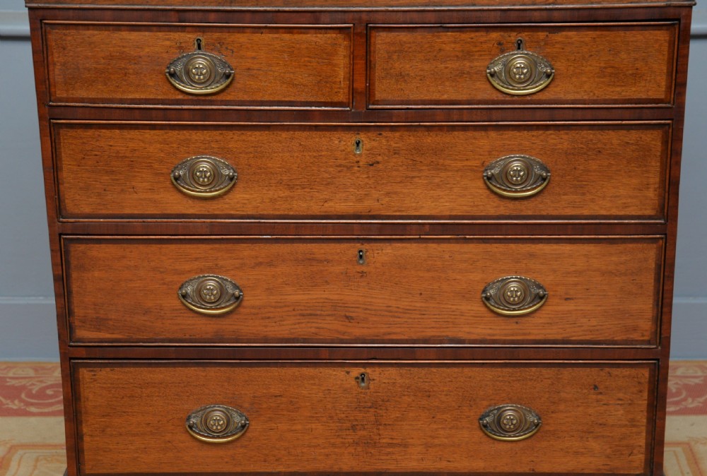 A George II solid oak chest of drawers featuring two short over three long graduated drawers with brass drop handles and bracket feet. View II