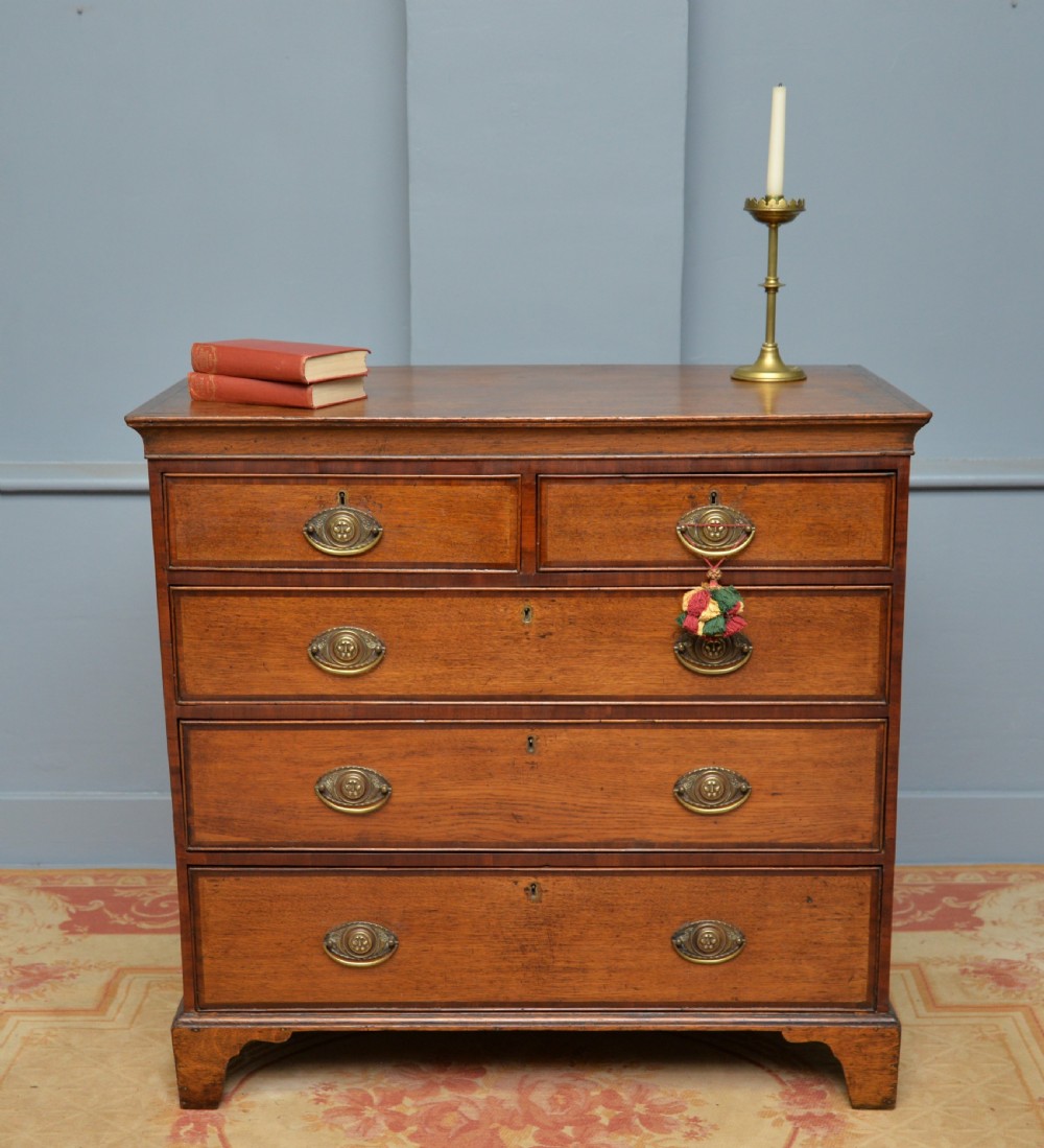 A George II solid oak chest of drawers featuring two short over three long graduated drawers with brass drop handles and bracket feet. View III