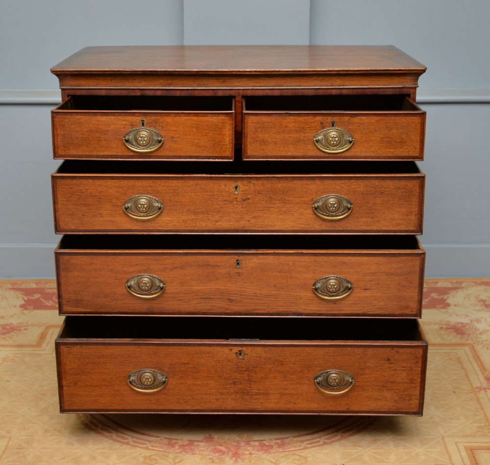 A George II solid oak chest of drawers featuring two short over three long graduated drawers with brass drop handles and bracket feet. View V