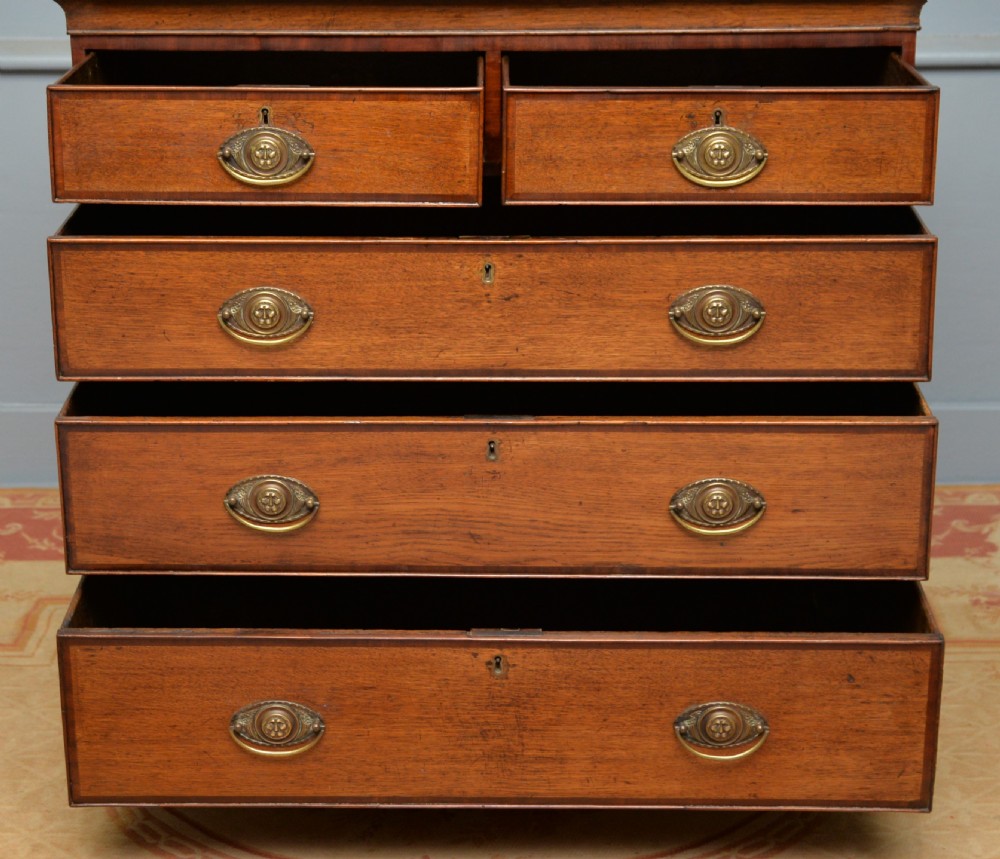 A George II solid oak chest of drawers featuring two short over three long graduated drawers with brass drop handles and bracket feet. View VI