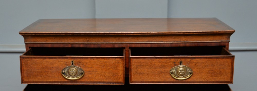 A George II solid oak chest of drawers featuring two short over three long graduated drawers with brass drop handles and bracket feet. View VII