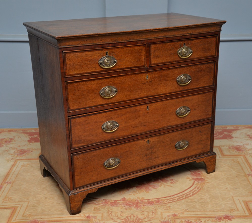 A George II solid oak chest of drawers featuring two short over three long graduated drawers with brass drop handles and bracket feet. View VIII