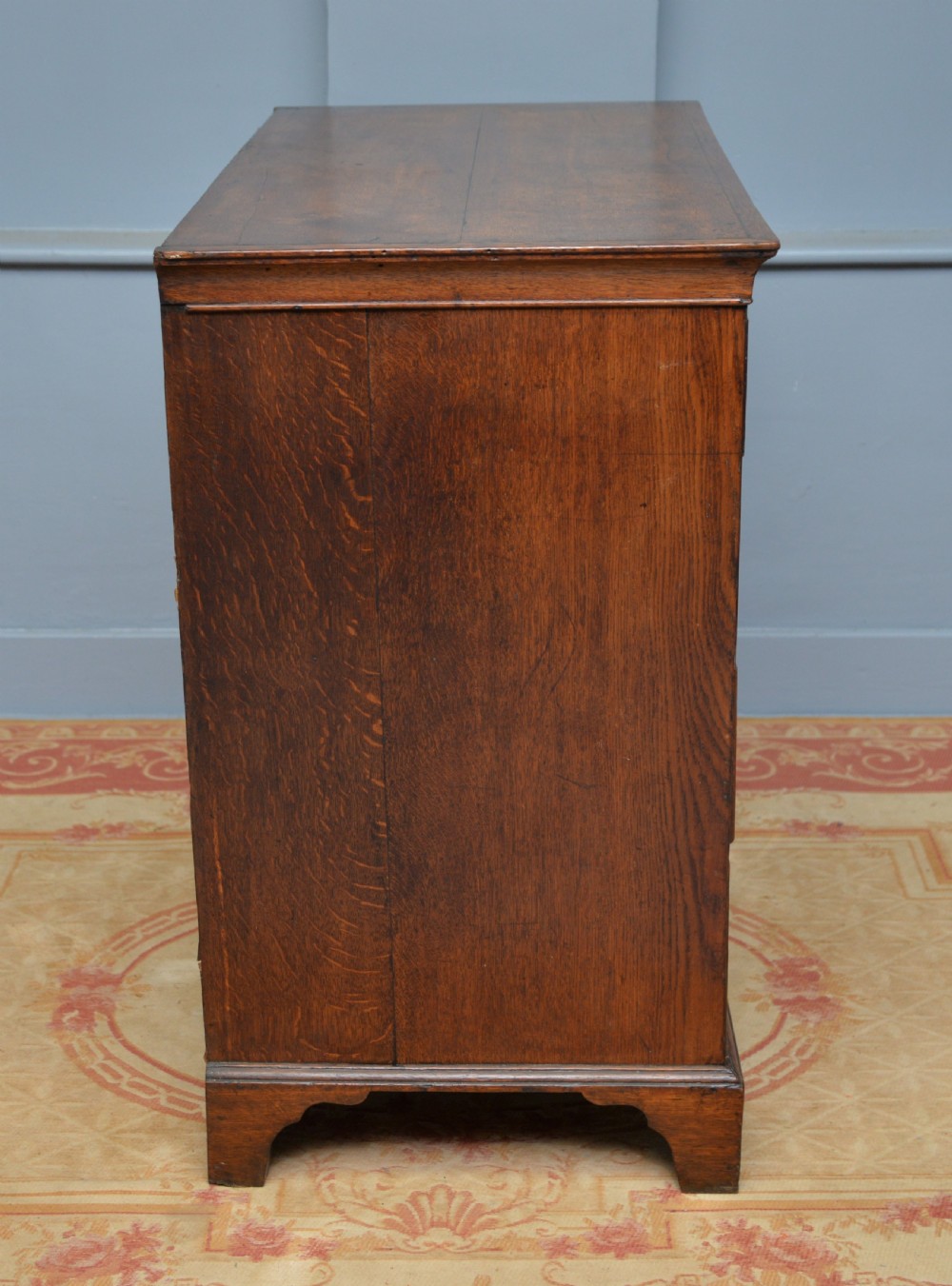 A George II solid oak chest of drawers featuring two short over three long graduated drawers with brass drop handles and bracket feet. View IX