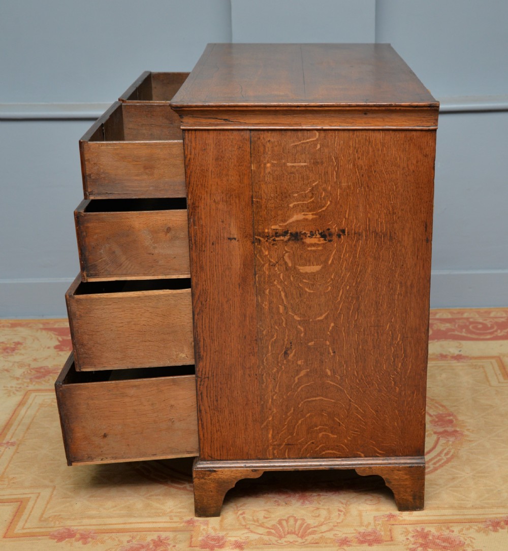 A George II solid oak chest of drawers featuring two short over three long graduated drawers with brass drop handles and bracket feet. View XI