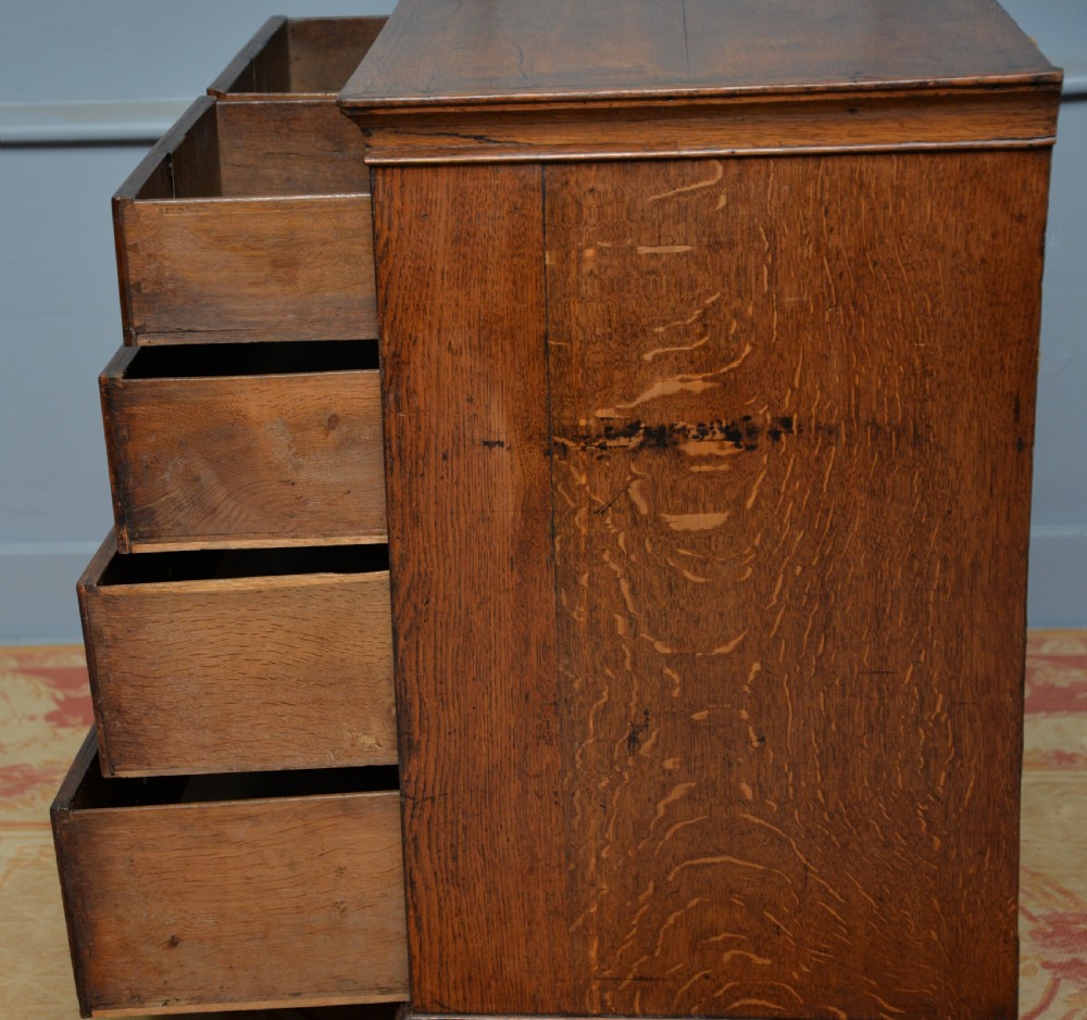A George II solid oak chest of drawers featuring two short over three long graduated drawers with brass drop handles and bracket feet. View XII