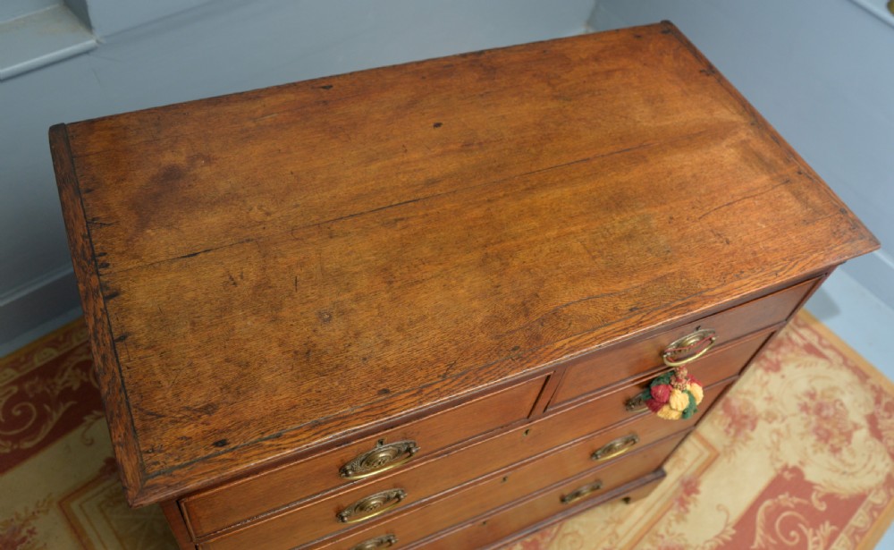 A George II solid oak chest of drawers featuring two short over three long graduated drawers with brass drop handles and bracket feet. View XIII