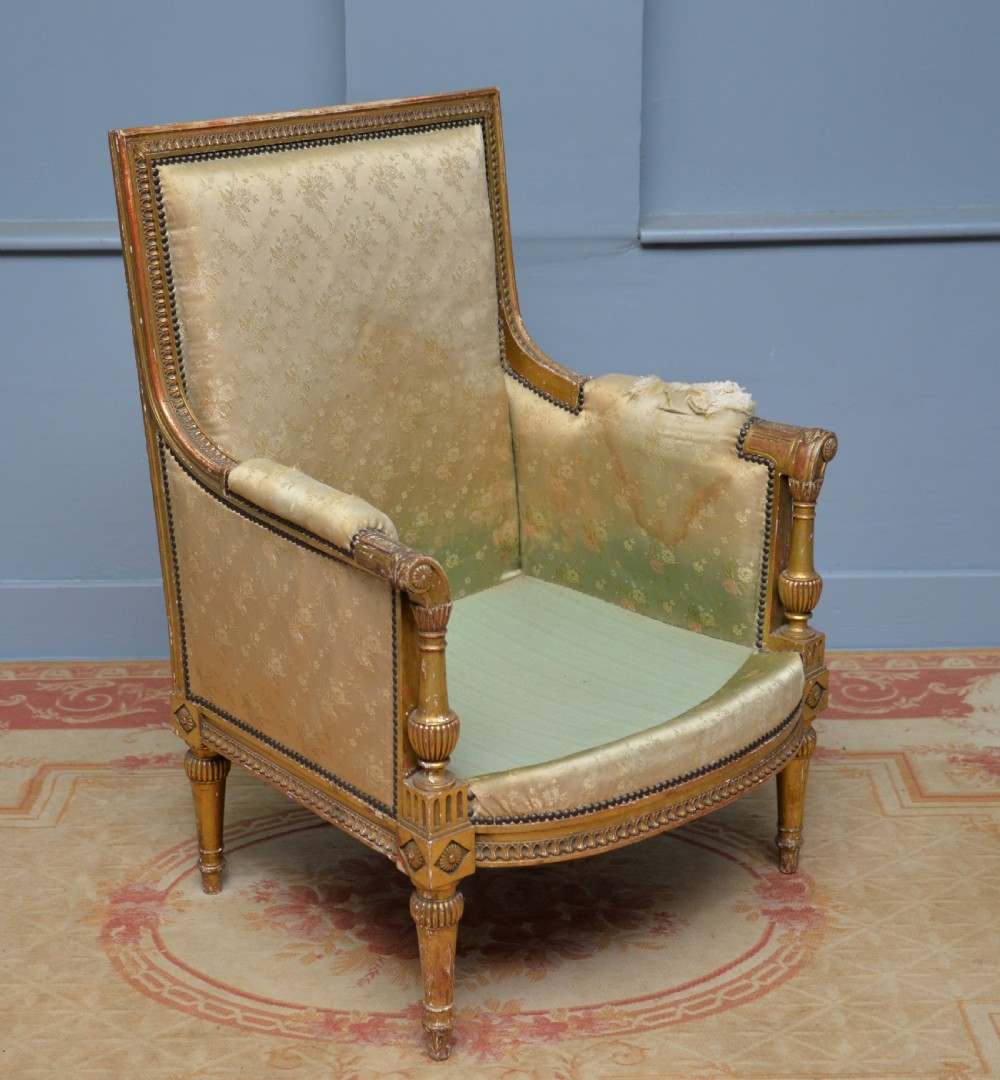 A 19th-century French Louis XVI style bergere armchair with a gilded carved wooden frame, fluted legs, and cream silk damask upholstery.