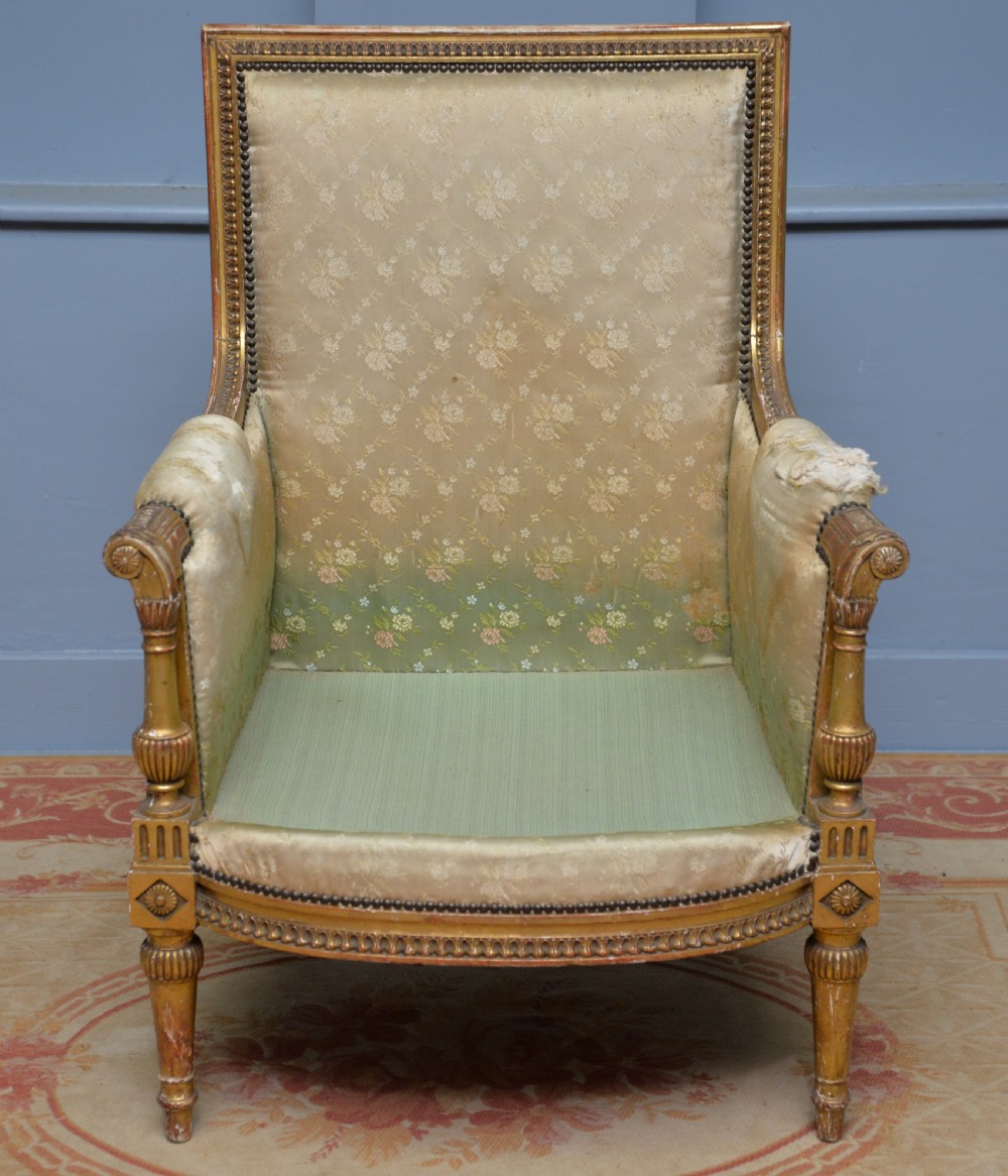 A 19th-century French Louis XVI style bergere armchair with a gilded carved wooden frame, fluted legs, and cream silk damask upholstery. View IV