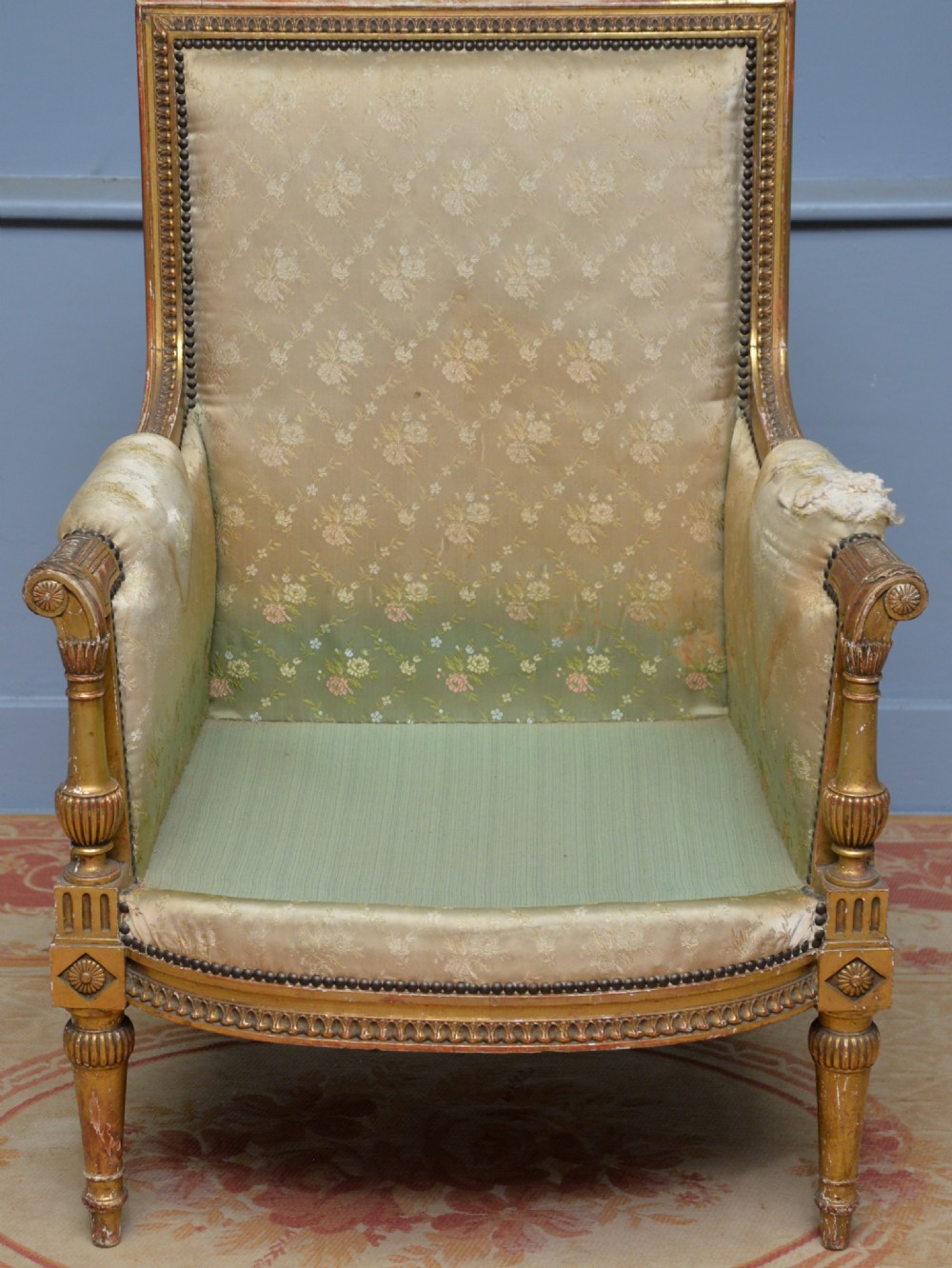 A 19th-century French Louis XVI style bergere armchair with a gilded carved wooden frame, fluted legs, and cream silk damask upholstery. View V