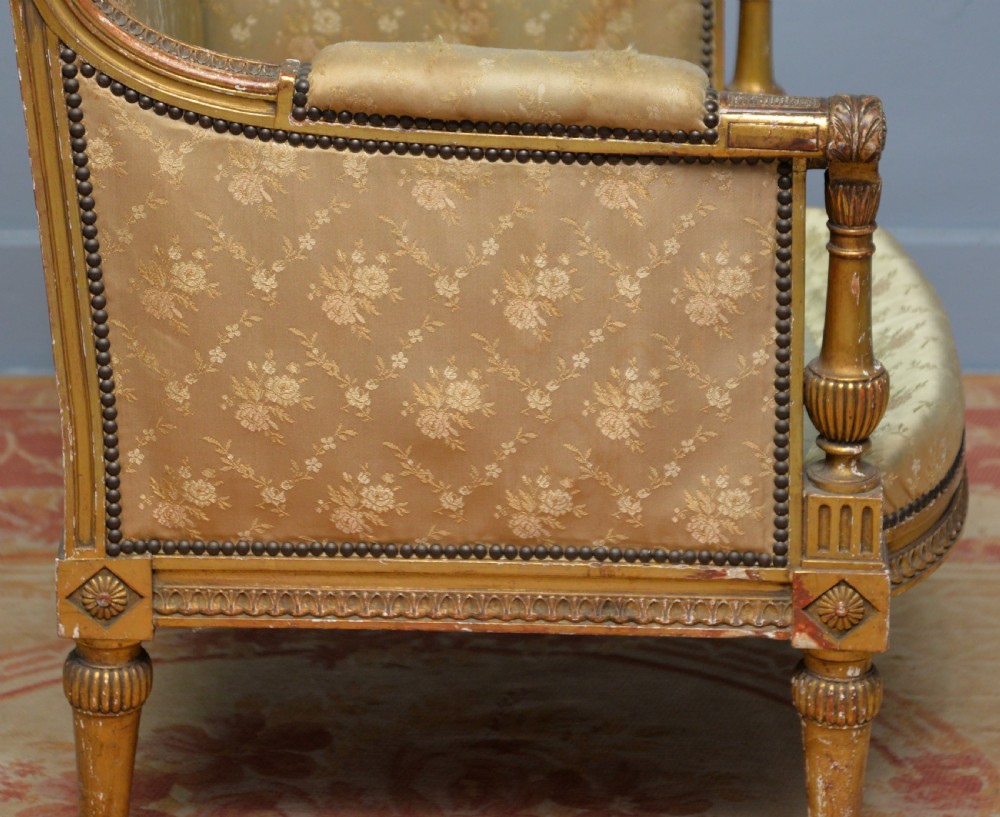 A 19th-century French Louis XVI style bergere armchair with a gilded carved wooden frame, fluted legs, and cream silk damask upholstery. View X