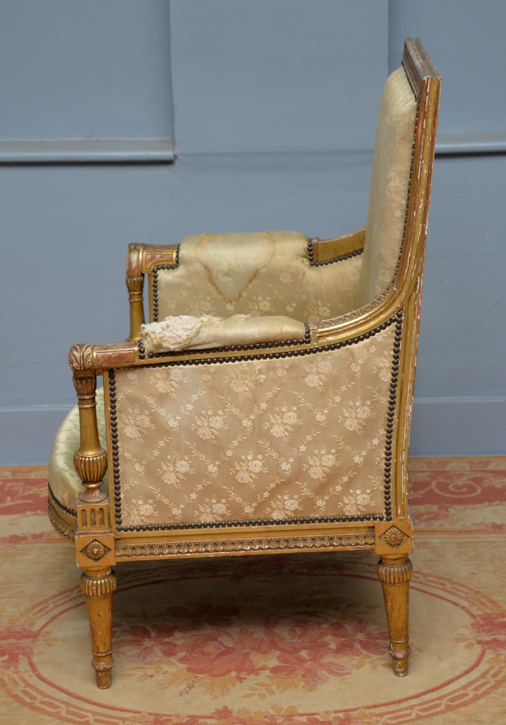 A 19th-century French Louis XVI style bergere armchair with a gilded carved wooden frame, fluted legs, and cream silk damask upholstery. View XII