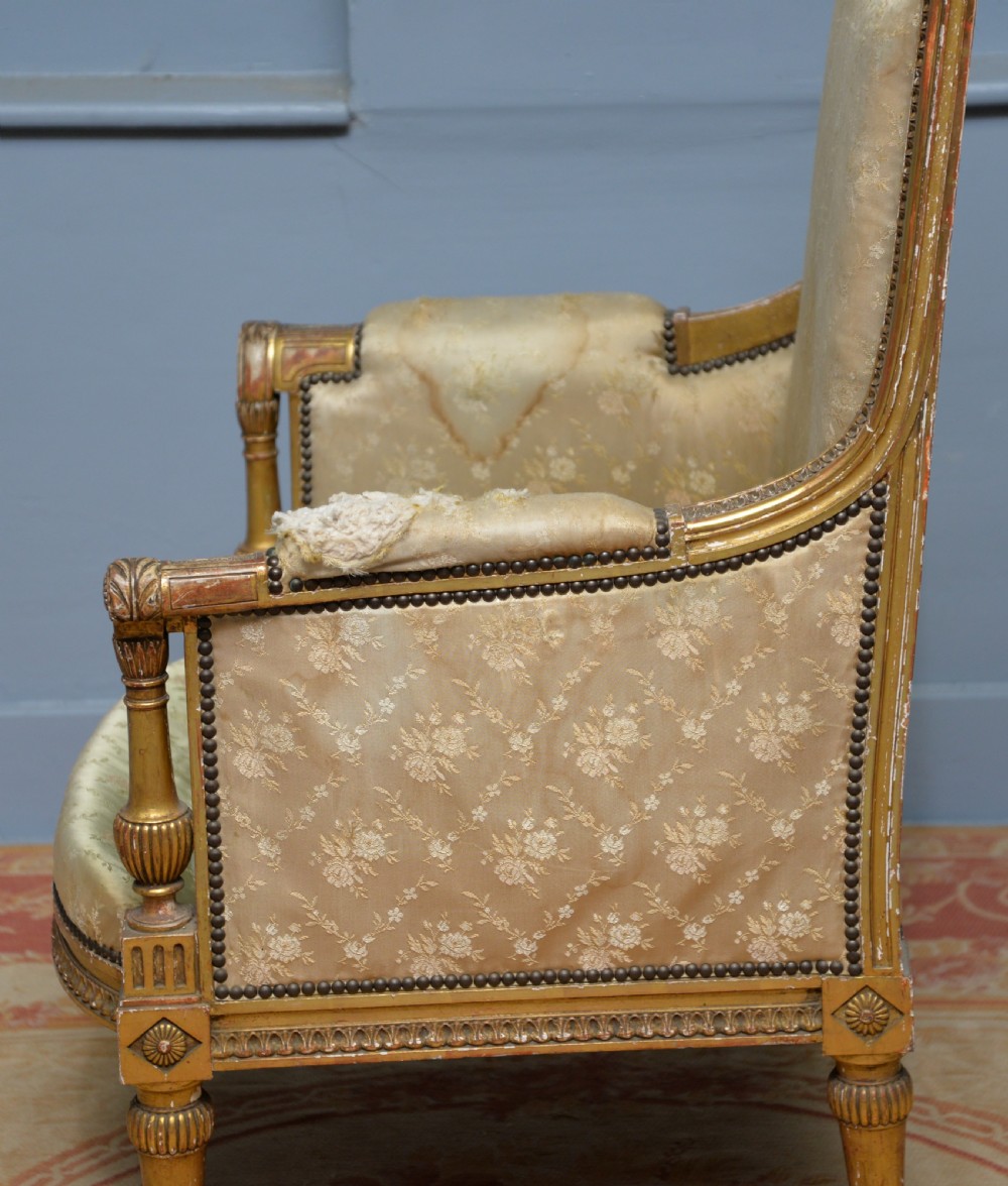 A 19th-century French Louis XVI style bergere armchair with a gilded carved wooden frame, fluted legs, and cream silk damask upholstery. View XIII