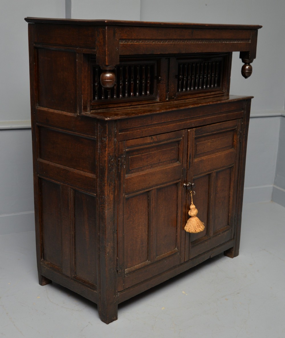 A dark oak 17th-century food court cupboard featuring an upper spindled section with drop finials above a lower two-door panelled cabinet.