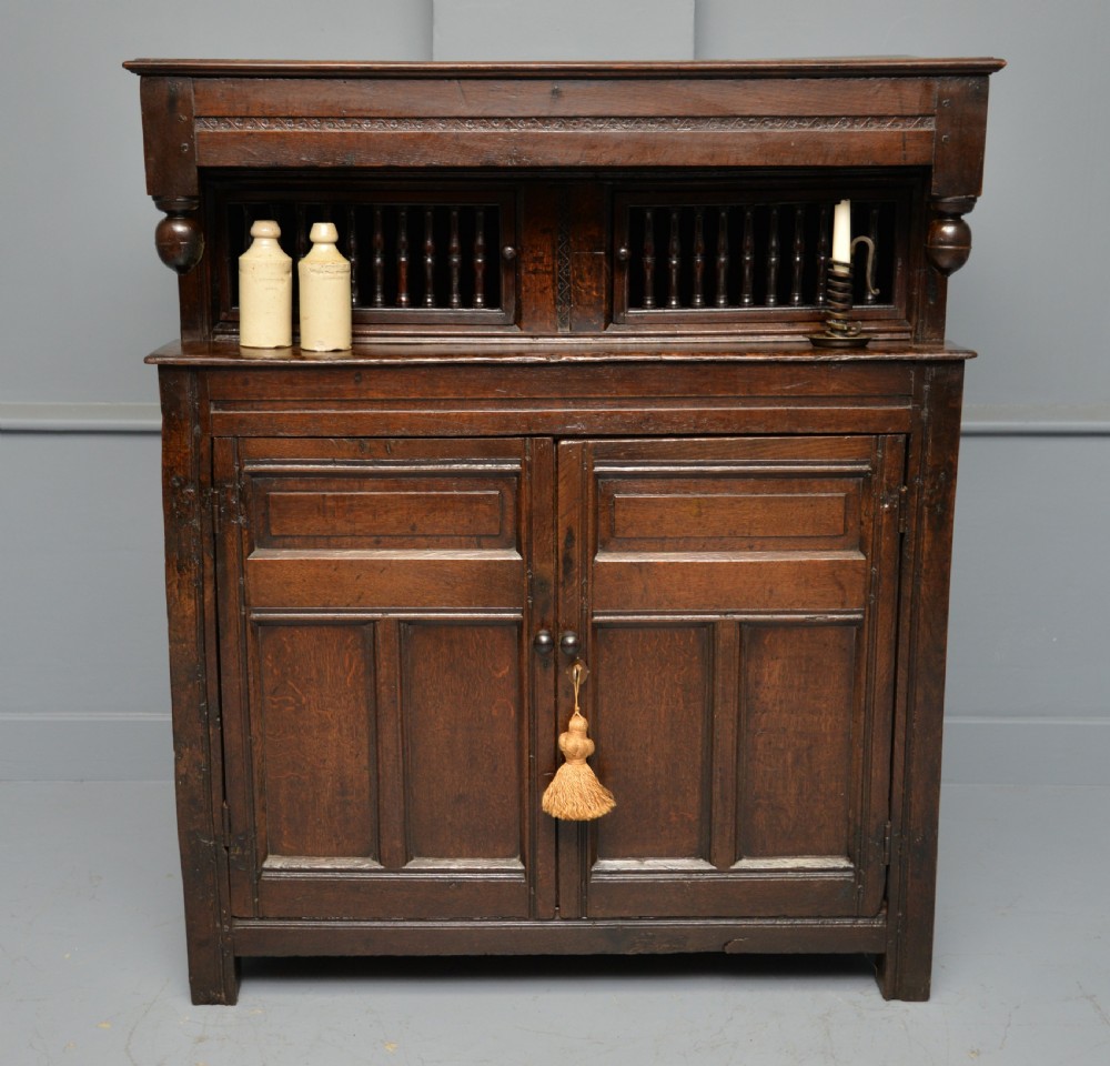 A dark oak 17th-century food court cupboard featuring an upper spindled section with drop finials above a lower two-door panelled cabinet. View II