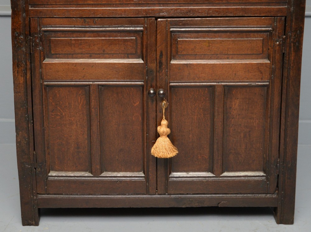 A dark oak 17th-century food court cupboard featuring an upper spindled section with drop finials above a lower two-door panelled cabinet. View IV