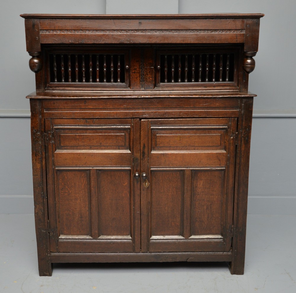 A dark oak 17th-century food court cupboard featuring an upper spindled section with drop finials above a lower two-door panelled cabinet. View V