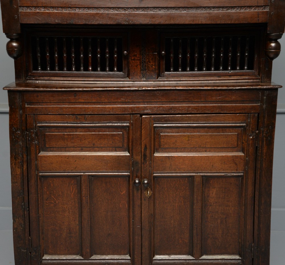 A dark oak 17th-century food court cupboard featuring an upper spindled section with drop finials above a lower two-door panelled cabinet. View VI