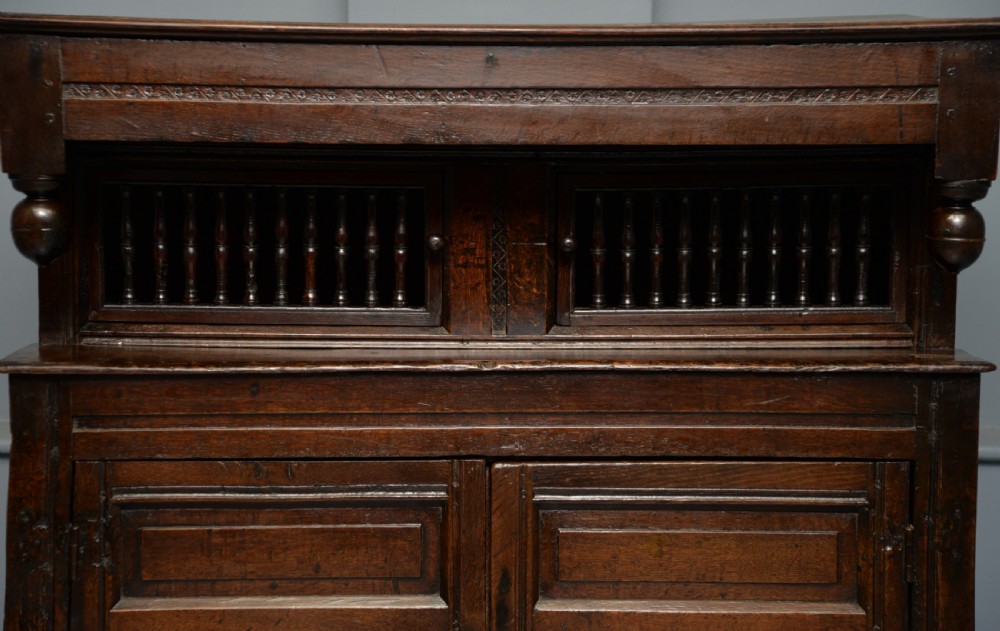 A dark oak 17th-century food court cupboard featuring an upper spindled section with drop finials above a lower two-door panelled cabinet. View VII