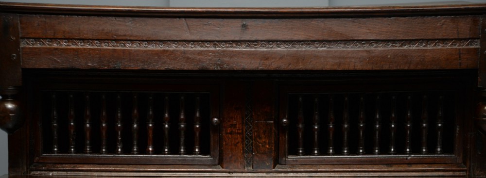 A dark oak 17th-century food court cupboard featuring an upper spindled section with drop finials above a lower two-door panelled cabinet. View VIII