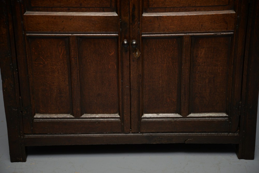 A dark oak 17th-century food court cupboard featuring an upper spindled section with drop finials above a lower two-door panelled cabinet. View IX