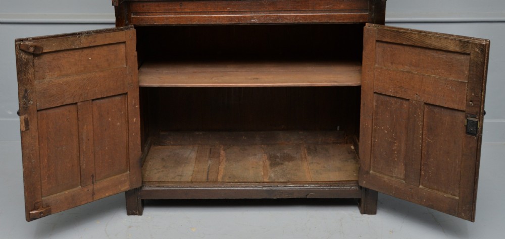 A dark oak 17th-century food court cupboard featuring an upper spindled section with drop finials above a lower two-door panelled cabinet. View X
