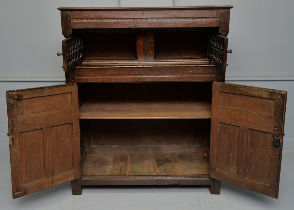 A dark oak 17th-century food court cupboard featuring an upper spindled section with drop finials above a lower two-door panelled cabinet. View XI