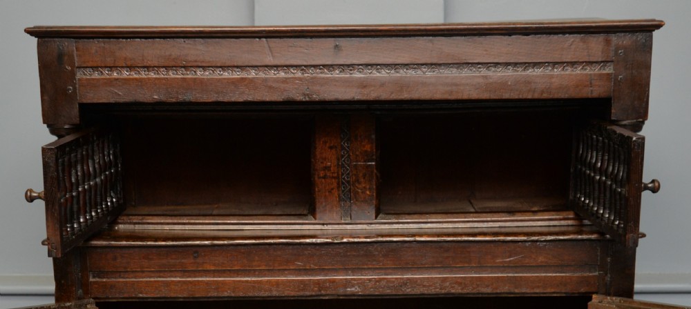 A dark oak 17th-century food court cupboard featuring an upper spindled section with drop finials above a lower two-door panelled cabinet. View XII