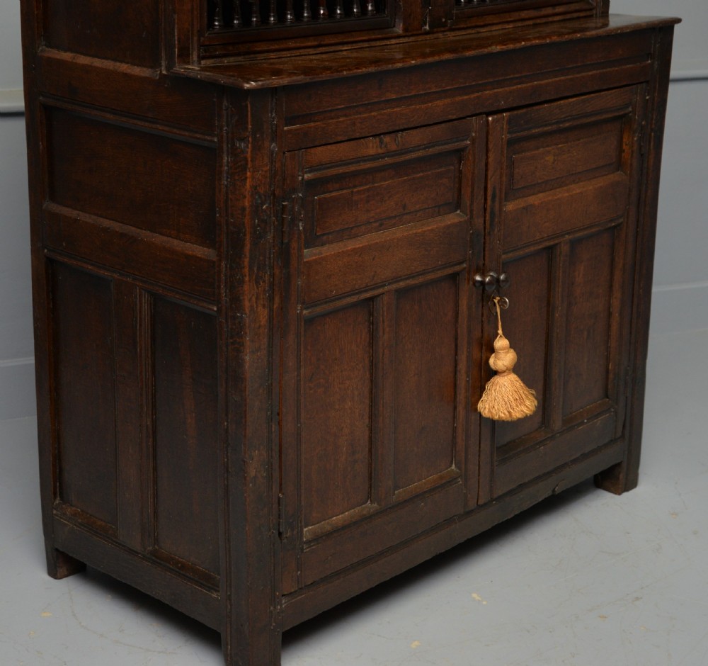 A dark oak 17th-century food court cupboard featuring an upper spindled section with drop finials above a lower two-door panelled cabinet. View XIV