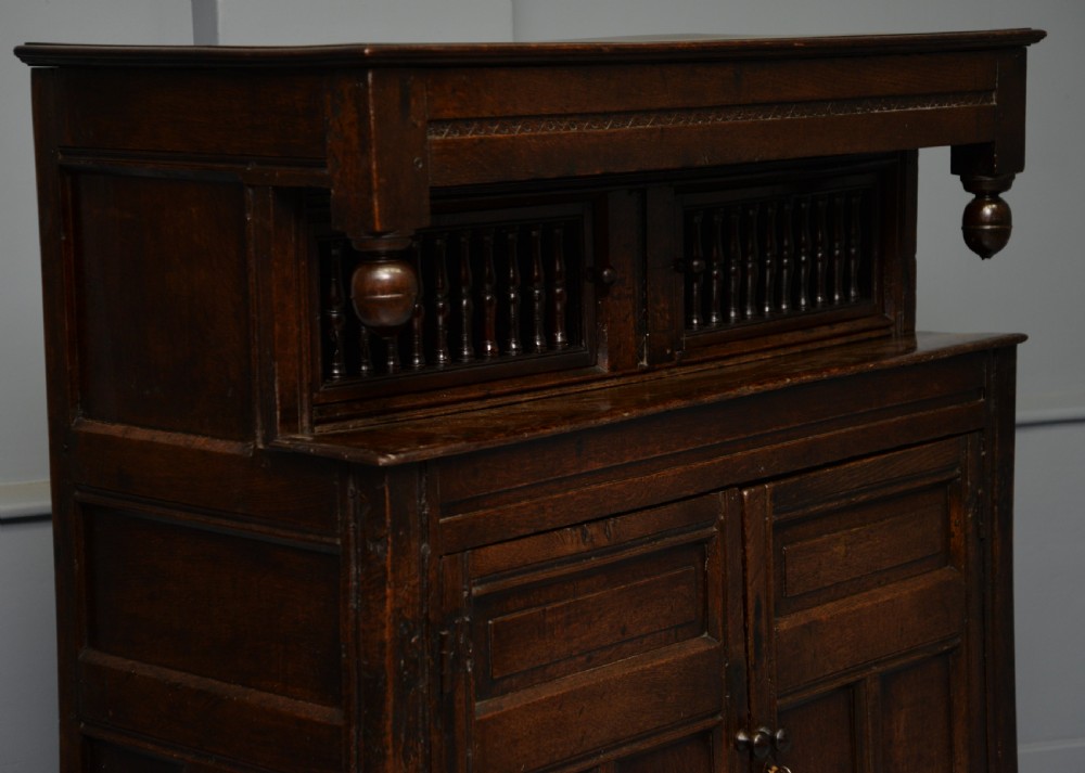 A dark oak 17th-century food court cupboard featuring an upper spindled section with drop finials above a lower two-door panelled cabinet. View XV