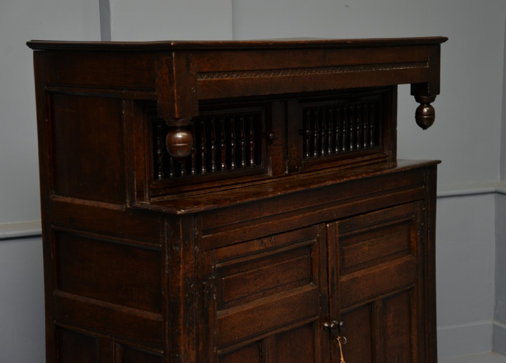 A dark oak 17th-century food court cupboard featuring an upper spindled section with drop finials above a lower two-door panelled cabinet. View XVI