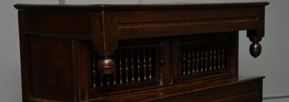 A dark oak 17th-century food court cupboard featuring an upper spindled section with drop finials above a lower two-door panelled cabinet. View XVII
