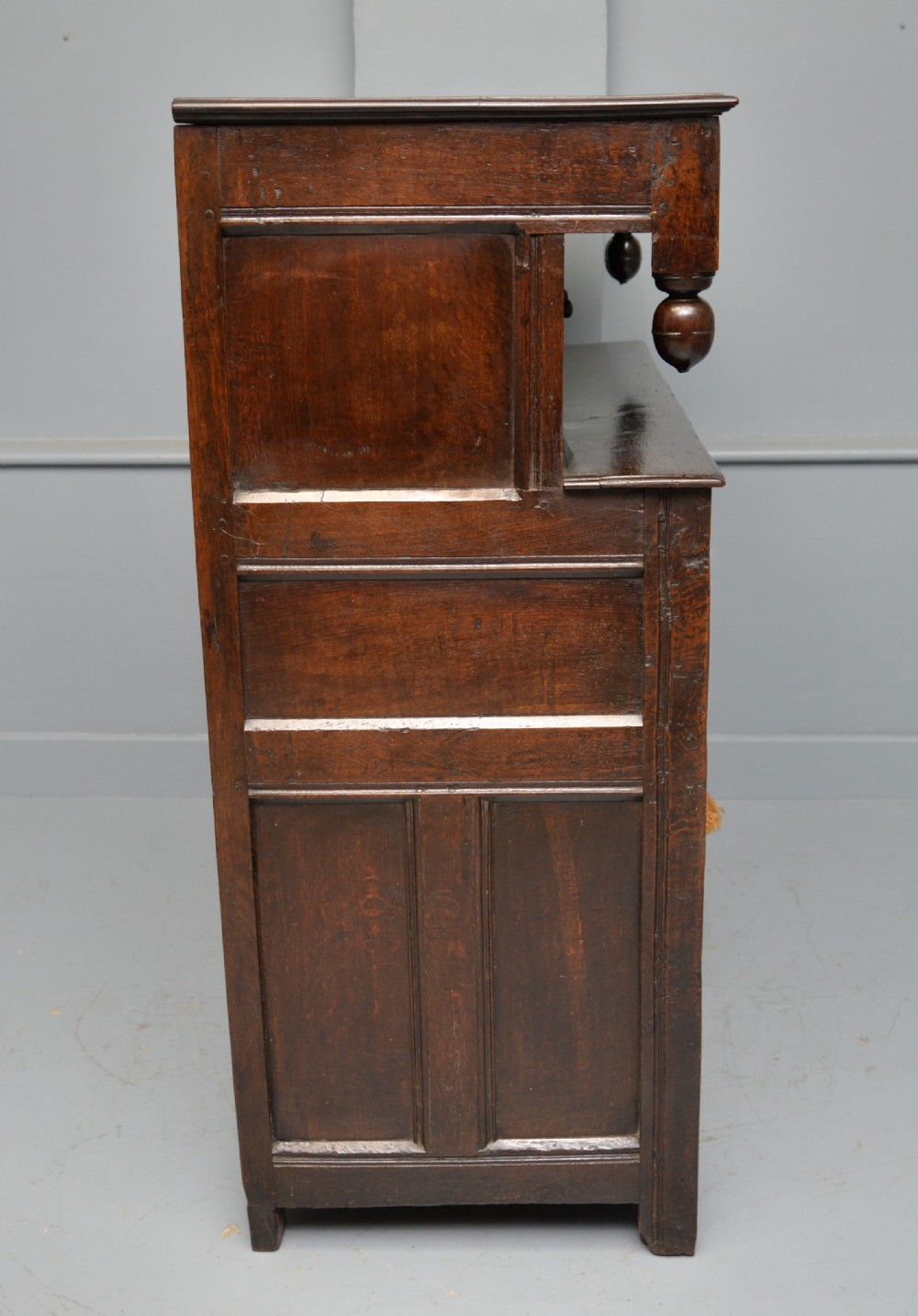 A dark oak 17th-century food court cupboard featuring an upper spindled section with drop finials above a lower two-door panelled cabinet. View XVIII