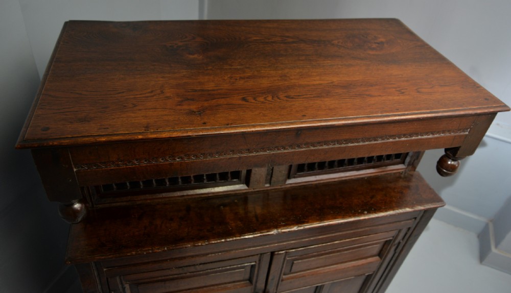 A dark oak 17th-century food court cupboard featuring an upper spindled section with drop finials above a lower two-door panelled cabinet. View XXI