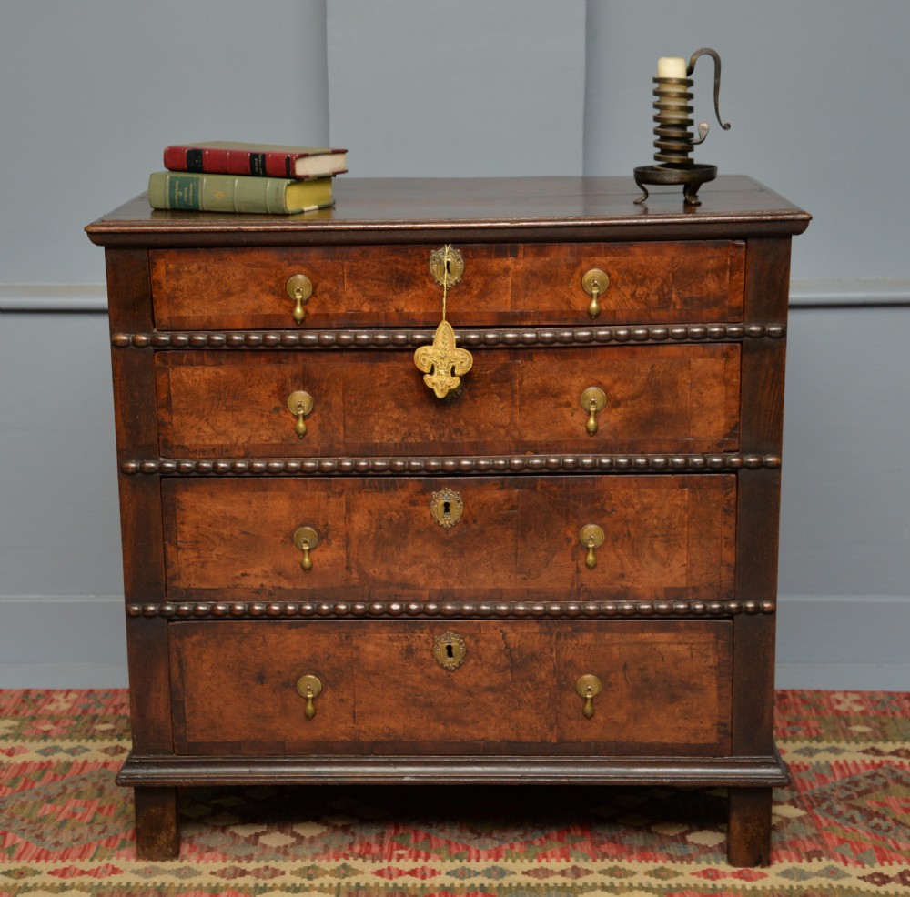 A William and Mary walnut and yew wood chest of four drawers featuring brass teardrop handles and decorative bead moulding. View II
