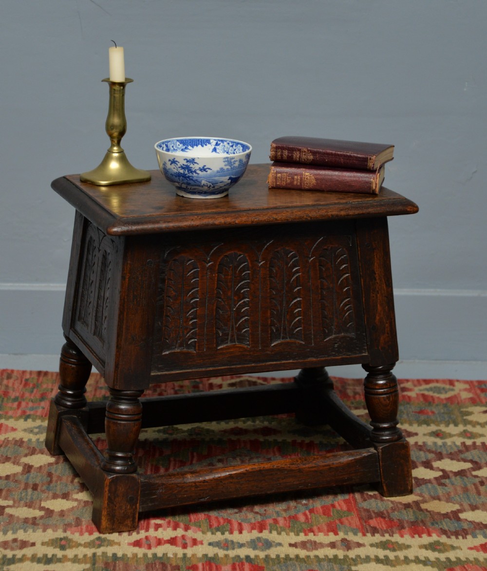A dark oak box stool featuring carved arched panels, turned baluster legs, and a rectangular top. View II