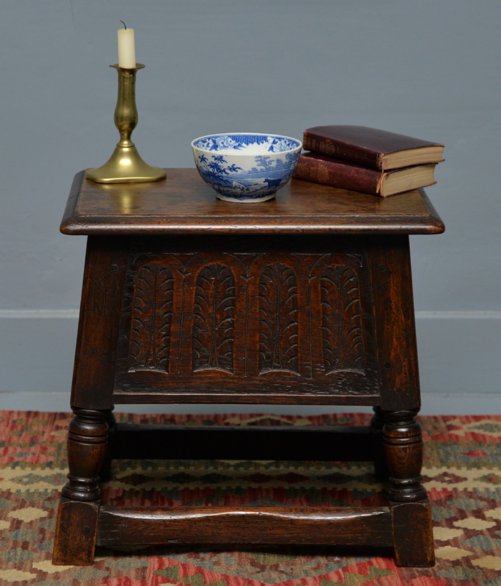 A dark oak box stool featuring carved arched panels, turned baluster legs, and a rectangular top. View III