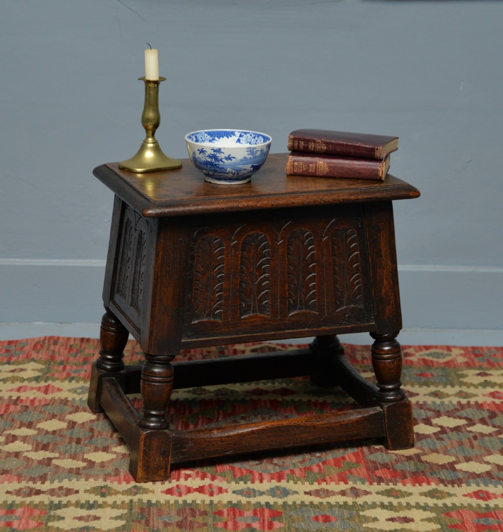 A dark oak box stool featuring carved arched panels, turned baluster legs, and a rectangular top. View IV